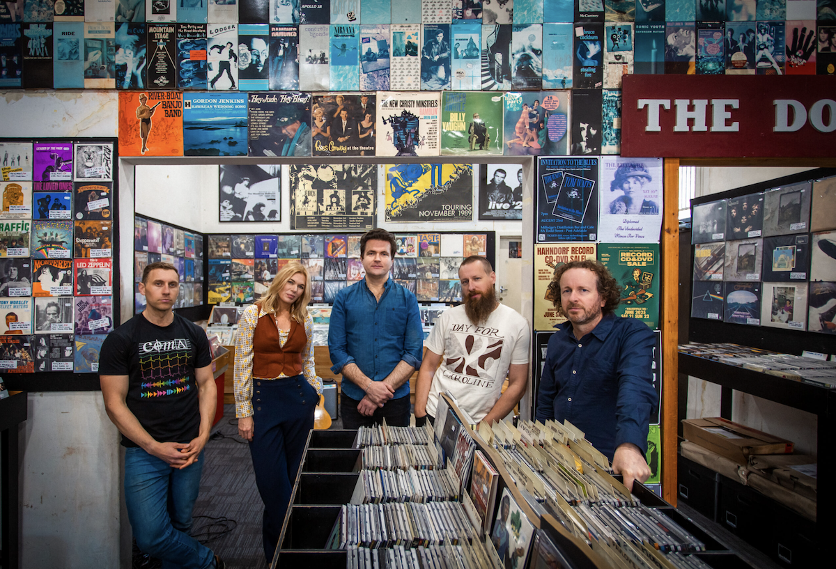 Band photo of Jen Lush & The Field standing inside a retro vinyl record shop surrounded by wall-to-wall album covers and record bins.